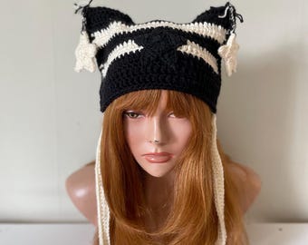 May include: A black and white striped crochet hat with star-shaped ear flaps and long ties. The hat is on a mannequin head with long, reddish-brown hair.