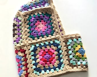 May include: A crocheted cowl with a geometric pattern of colorful squares. The cowl is made of beige yarn with multi-colored squares in shades of pink, blue, green, purple, and yellow.