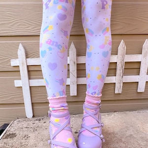 May include: Light purple platform shoes with criss-cross straps and buckle closures. The shoes are paired with light purple leggings patterned with hearts, stars, and the words "Precious Fancy Us". Pink socks with a ruffled edge complete the look.