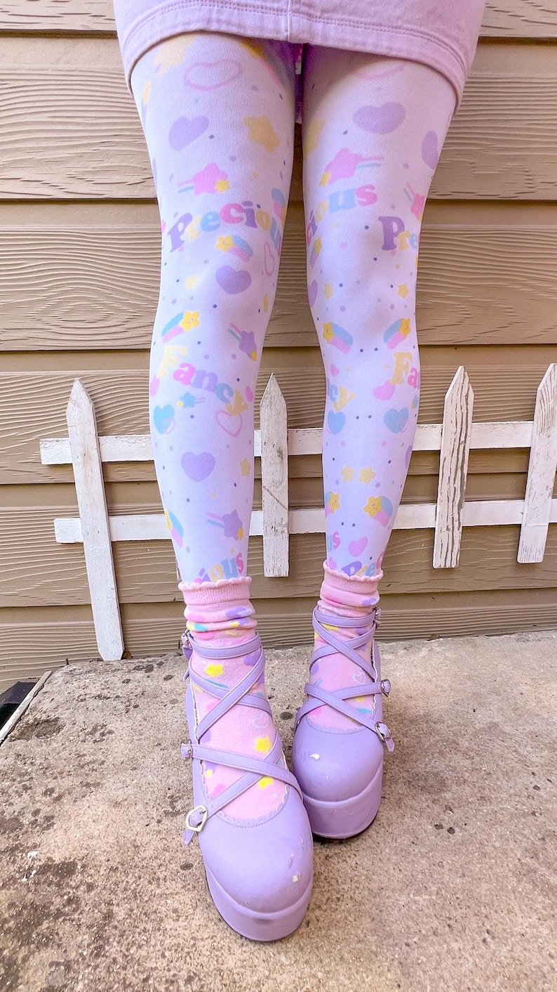 May include: Light purple platform shoes with criss-cross straps and buckle closures. The shoes are paired with light purple leggings patterned with hearts, stars, and the words "Precious Fancy Us". Pink socks with a ruffled edge complete the look.