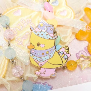 May include: A yellow chick wearing a purple and blue cowboy hat with stars and a purple and blue bandana with stars. The chick is wearing pink boots and has a pink bow on its tail.