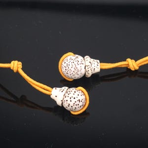 May include: Two white and brown speckled beads with a yellow elastic cord. The beads are round and have a small, pointed top.