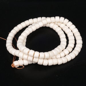 Op de afbeelding: Een witte kralenketting met een bruin koord. De kralen zijn rond en hebben een gladde, gepolijste afwerking.