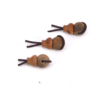 Peut inclure: Trois perles en bois brun avec un cordon brun attaché à chacune. Les perles sont rondes avec un petit sommet légèrement pointu.