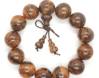 May include: A wooden beaded bracelet with a natural wood grain pattern. The bracelet features large, round beads in shades of brown and tan, strung together with a decorative wooden clasp and tassel. The beads are approximately 1 inch in diameter.