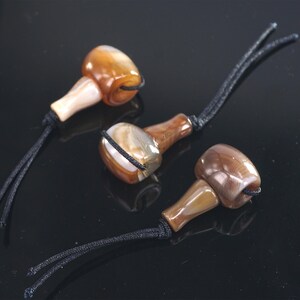 May include: Three brown and white agate beads with black cords. The beads are teardrop shaped and have a polished finish.