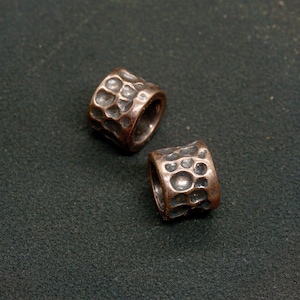 May include: Two copper-colored metal beads with a hammered texture. The beads are cylindrical in shape and have a hole through the center.