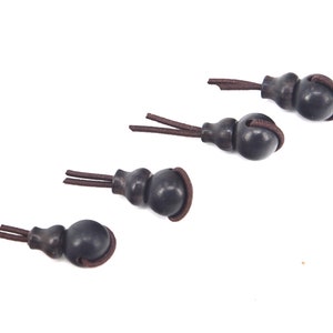 May include: Four brown gourd-shaped charms with brown cords. The charms are tied together in a row.