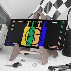 May include: Black license plate with a green, orange, and blue design and the text "TETC" in white letters.