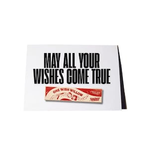 May include: A white greeting card featuring the black text "MAY ALL YOUR WISHES COME TRUE" above a rectangular red and white graphic label that reads "ONE WISH WILLOW" with an illustration of a person and the text "AMAZE YOUR FRIENDS".