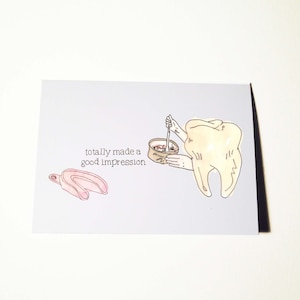 Può includere: Biglietto di auguri azzurro chiaro a tema dentale. La carta presenta un dente dei cartoni animati che tiene una ciotola con un cucchiaio, un portaimpronta dentale rosa e il testo "totally made a good impression."