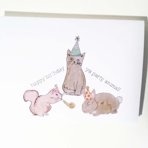 May include: A birthday card with a watercolor illustration of a cat, squirrel, and rabbit wearing party hats. The text on the card reads "happy birthday ya party animal!"