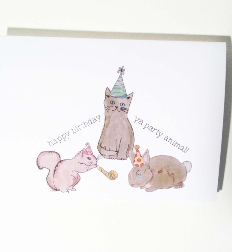May include: A birthday card with a watercolor illustration of a cat, squirrel, and rabbit wearing party hats. The text on the card reads "happy birthday ya party animal!"
