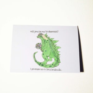 Puede incluir: Tarjeta de felicitación blanca con una ilustración de Godzilla verde con una corona de flores y un ramo. El texto dice: "¿Quieres ser mi dama de honor?" y "Prometo no ser una bridezilla."