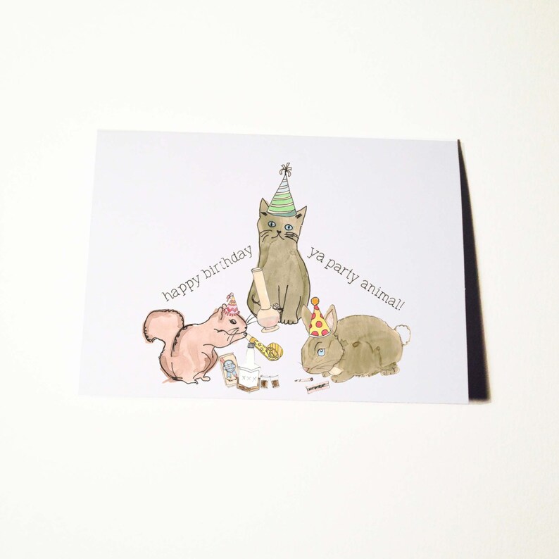 May include: A birthday card with a cat, squirrel, and rabbit wearing party hats. The cat is holding a bong and the squirrel is holding a birthday cake. The text on the card reads "happy birthday ya party animal!"