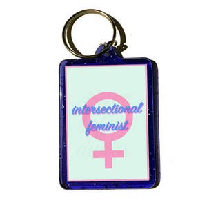 May include: A blue keychain with a pink female symbol and the text "intersectional feminist" on a light blue background.