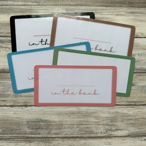 May include: A set of six blank cards with colorful borders. The cards have the text "in the bank" written on them in cursive.