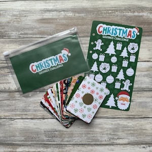 May include: A green zippered pouch with the text "Christmas Savings Challenge" in white and blue letters. A stack of colorful cards with snowflakes and Christmas designs. A green card with the text "Christmas Savings Challenge" in white and blue letters and various Christmas-themed stickers.