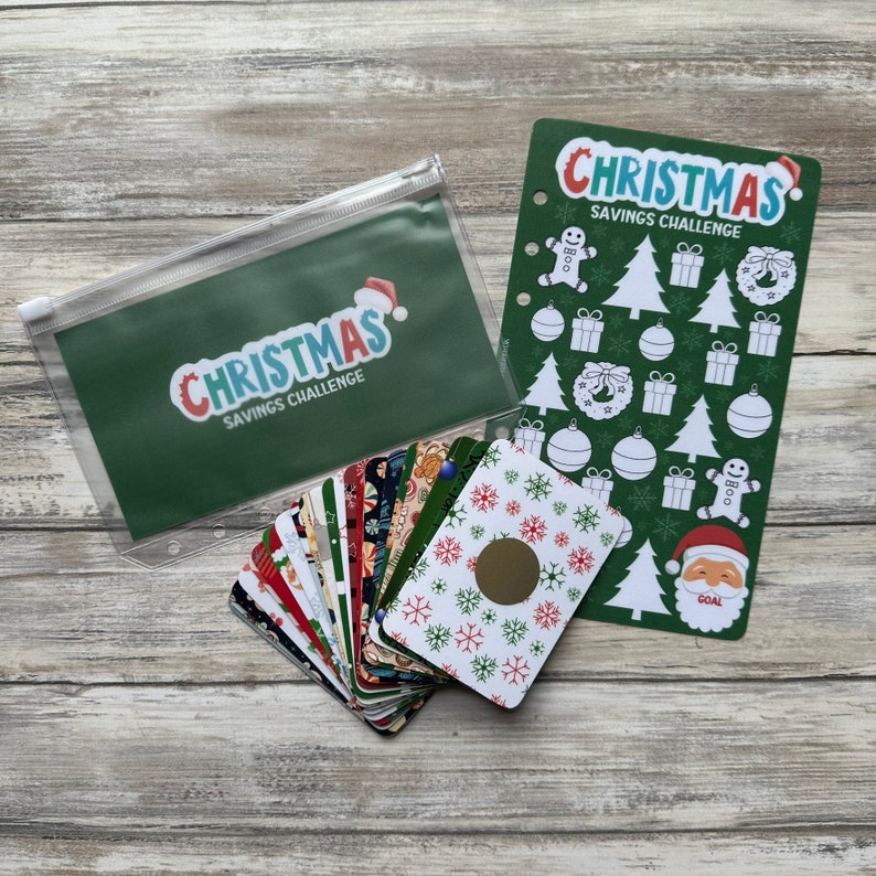 May include: A green zippered pouch with the text "Christmas Savings Challenge" in white and blue letters. A stack of colorful cards with snowflakes and Christmas designs. A green card with the text "Christmas Savings Challenge" in white and blue letters and various Christmas-themed stickers.