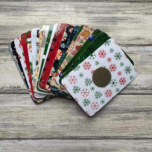 May include: A stack of colorful Christmas cards with a snowflake design and a gold circle in the center. The cards are arranged in a fan shape.