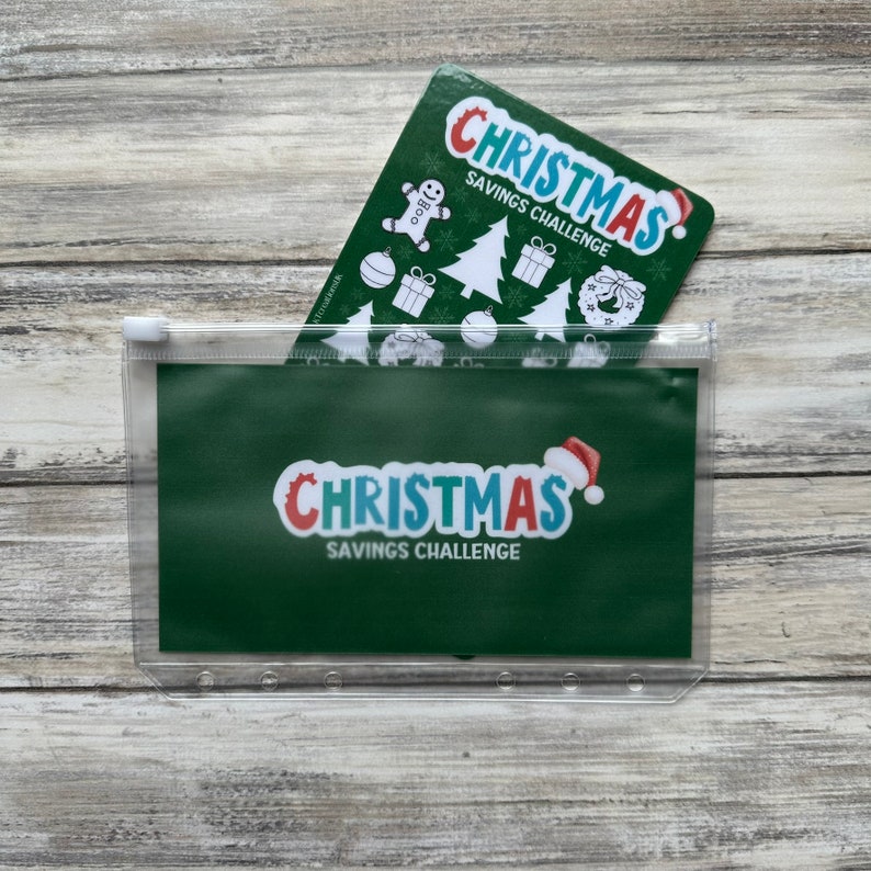 May include: A clear plastic zippered pouch with a green background and the text "Christmas Savings Challenge". A smaller card with the same text and a Christmas-themed design is visible inside the pouch.