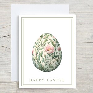 May include: Easter greeting card featuring a watercolor illustration of an egg adorned with pink flowers and green foliage. The card has a white background with a green border and the words "HAPPY EASTER".