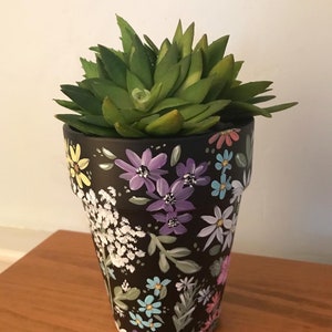 May include: A black planter pot with a floral design painted on it. The pot is filled with a green succulent plant.