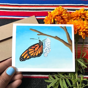 May include: A watercolor painting of a monarch butterfly emerging from its chrysalis. The butterfly is orange, black, and white, and the chrysalis is white. The painting is set against a blue sky background.