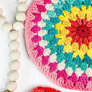 May include: Two colorful crocheted round mats with a rainbow gradient pattern. The larger mat is pink, turquoise, yellow, and red. The smaller mat is red, yellow, and orange.