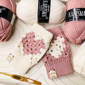 Op de afbeelding: Twee gebreide vingerloze handschoenen met een roze en wit granny square patroon. De handschoenen zijn gemaakt met Drops Karisma garen en hebben een Lullaby Lodge label.