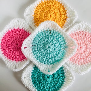 May include: Five crocheted squares in different colors. The squares are white with a center circle in pink, yellow, teal, and two shades of green.