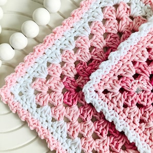 May include: A pink and white crochet baby blanket with a gradient of pink shades. The blanket is made with a square stitch pattern.