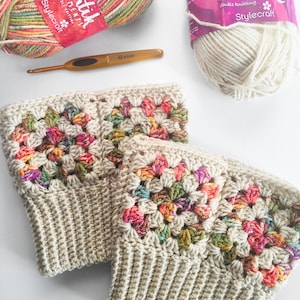 Puede incluir: Dos calentadores de piernas de ganchillo con una base beige y un patrón de granny squares colorido. La lana es una mezcla multicolor de rosa, naranja, verde y morado. Los calentadores de piernas están hechos con un gancho de ganchillo etiquetado "G 4.0mm".