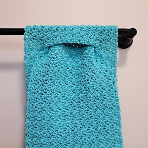 May include: A turquoise crocheted dish towel with white crocheted stripes at the bottom. The towel is hanging on a black towel rack.
