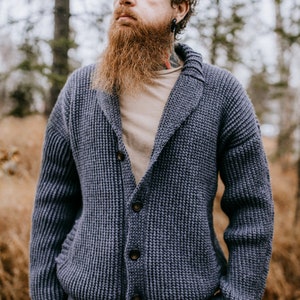 May include: A blue knitted cardigan with a shawl collar and button closure. The cardigan is made with a textured stitch and has a relaxed fit.