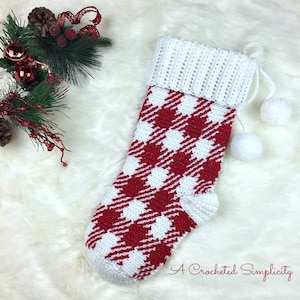 May include: Red and white crocheted Christmas stocking with a white pom-pom on the top. The stocking has a gingham pattern and is decorated with two white pom-poms. "A Crocheted Simplicity" is written in cursive at the bottom of the stocking.