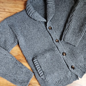 May include: A gray knitted cardigan with a large collar, button closure, and a pocket on the left side.