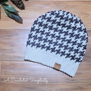 May include: A white and gray crocheted beanie with a houndstooth pattern. The beanie has a brown leather tag with the word "Hop" on it.