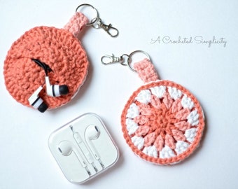 Puede incluir: Dos porta auriculares de ganchillo con llaveros. Los porta auriculares son redondos y están hechos con hilo rosa y blanco. El texto "A Crocheted Simplicity" es visible en la esquina superior derecha de la imagen.