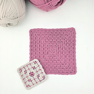 May include: A square, dusty rose crochet piece with a textured pattern, next to a smaller, similar piece in gray and pink. Two balls of yarn, one gray and one pink, are in the background. The items are likely for a crochet project.