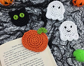 May include: Handmade crochet Halloween decorations. The image shows a black cat with green eyes, two white ghosts, and an orange pumpkin with a green stem. They are arranged on black mesh fabric.