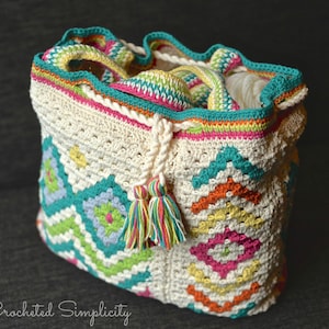 May include: A white crocheted tote bag with a colorful geometric pattern. The bag has a drawstring closure and a tassel.