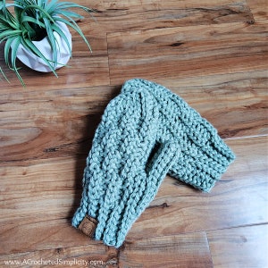 May include: A teal blue crocheted infinity scarf with a brown leather tab. The scarf is made with a cable stitch pattern.