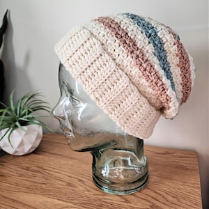 May include: A crocheted beanie with a cream base and stripes of brown, blue, and white.