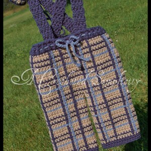 May include: Crocheted baby trousers with a plaid pattern in blue and beige. The trousers have braces and a bow tie.