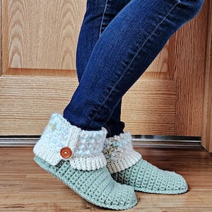 May include: A pair of green crocheted slippers with white and light blue crocheted cuffs. The slippers have a brown button on the cuff.