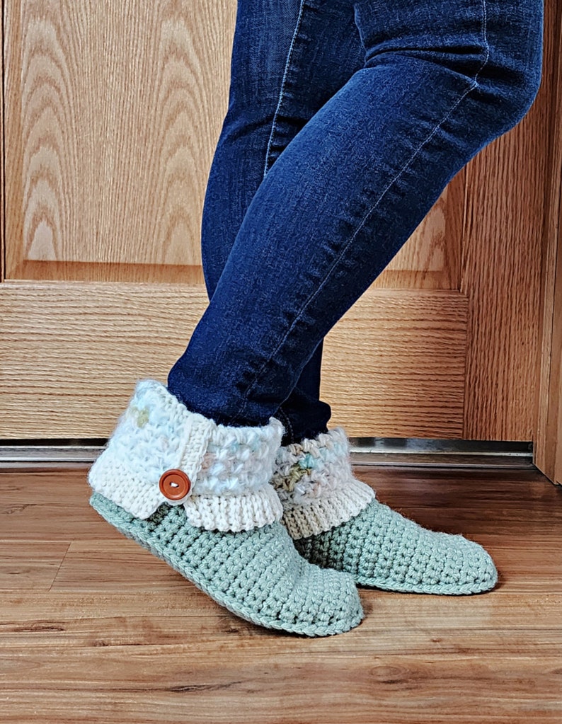 May include: A pair of green crocheted slippers with white and light blue crocheted cuffs. The slippers have a brown button on the cuff.