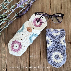 May include: Two crocheted eyeglass cases in a granny square pattern. One is open, displaying a pair of glasses, and the other is closed. The open case is cream-colored with blue and purple accents, and a wooden button closure. The closed case is blue and white.