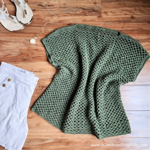 May include: A green crochet top with a loose, open weave. The top is laid flat on a wooden surface.