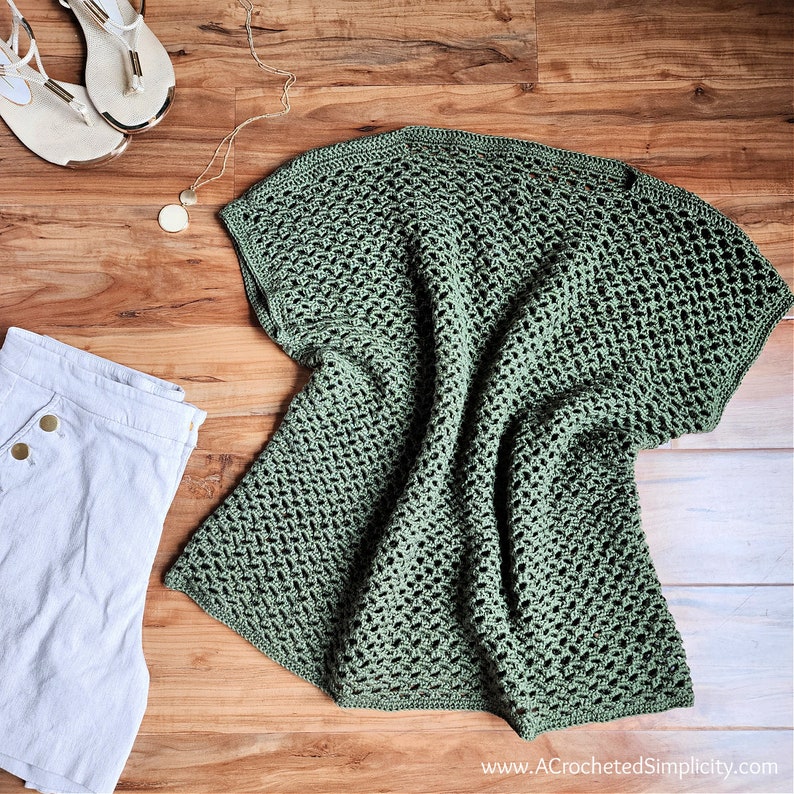 May include: A green crochet top with a loose, open weave. The top is laid flat on a wooden surface.